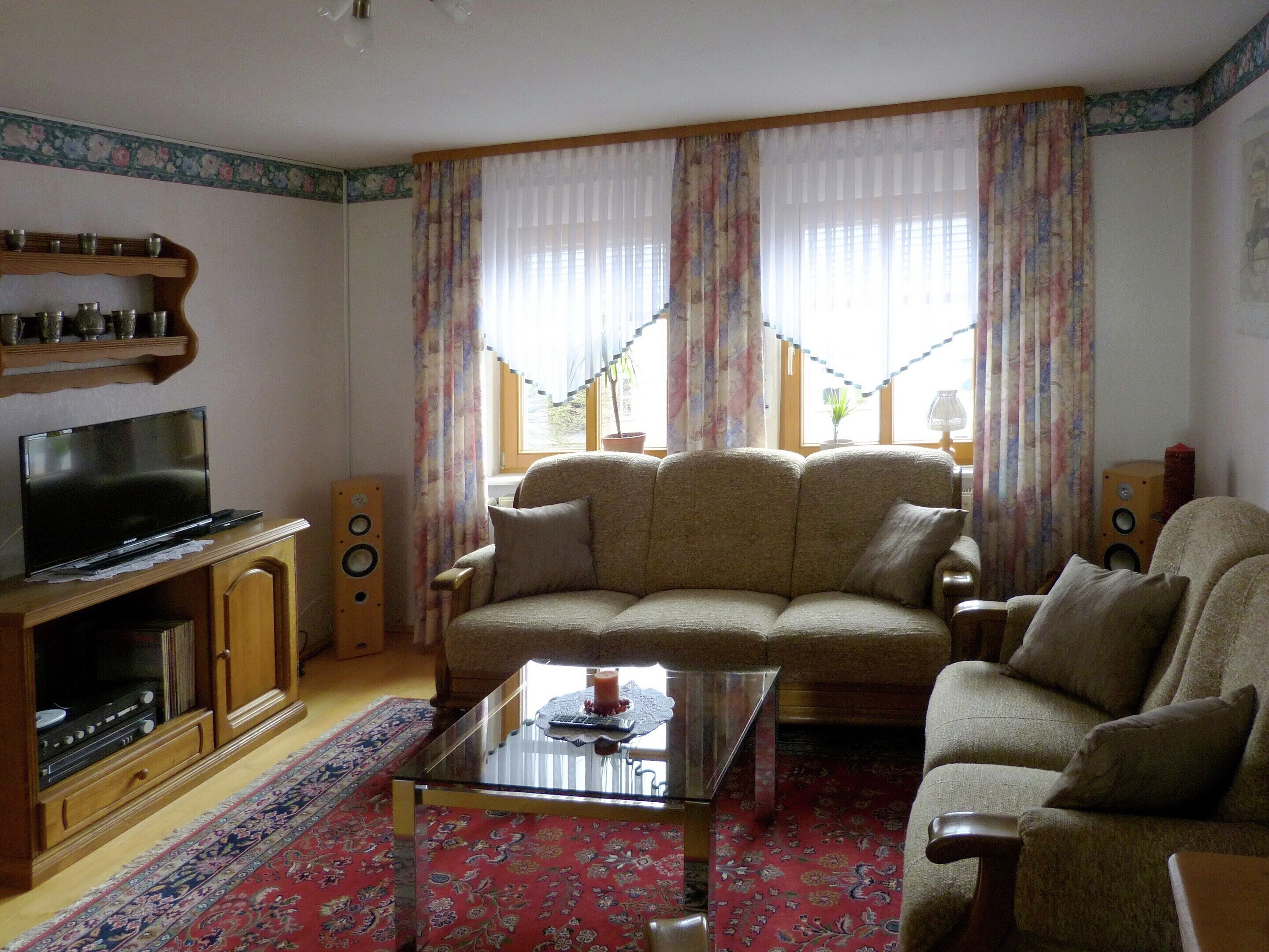 Un soggiorno con un divano, un tavolino, una TV, degli altoparlanti e un tappeto decorato.