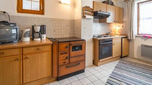 A compact kitchen with wooden cabinets, a stove, a microwave, and a television. - Retreat in the Ammergau Alps (Unterammergau)