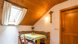 A cozy room with a wooden ceiling, a wooden cross on the wall, a dining table with chairs, and a wooden door. - Retreat in the Ammergau Alps (Unterammergau)