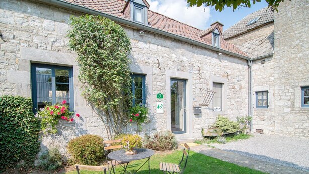 A stone building with a courtyard, a small round table, two chairs, and a bench. - Traditional Cottage With Private Terrace (Durbuy)