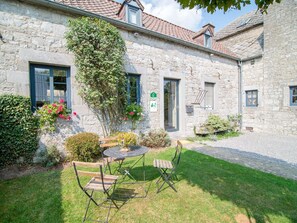 A stone building with a courtyard, a small round table, two chairs, and a bench. - Traditional Cottage With Private Terrace (Durbuy)