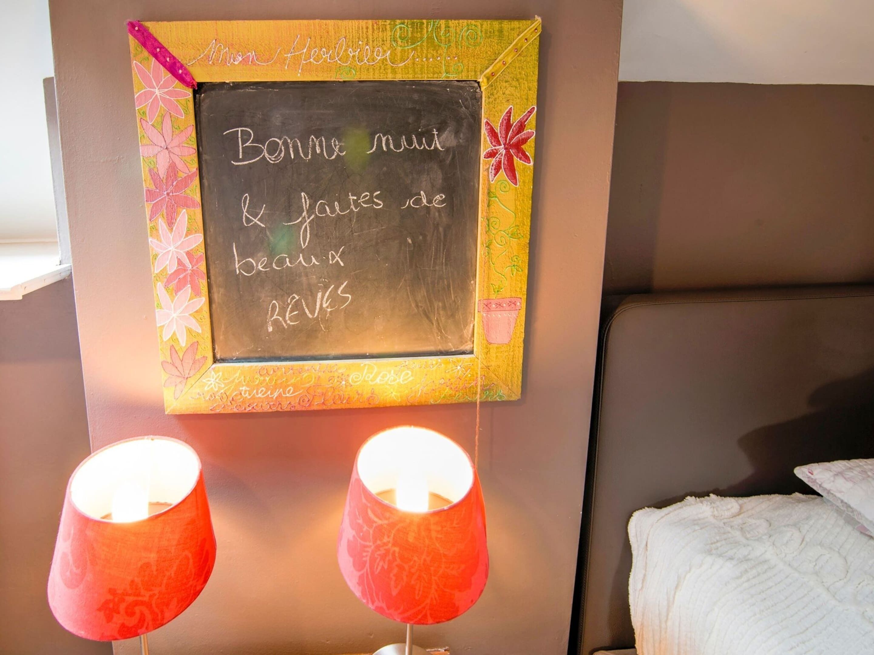 Ein Zimmer mit einer Tafel, auf der eine französische Nachricht steht, zwei roten Lampen und einem Bett mit weißer Bettdecke.