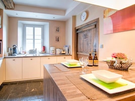 Una cocina con encimera de madera, un fregadero y diversos electrodomésticos. Hay una ventana, una puerta y un reloj en la pared.