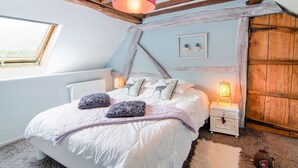 A bedroom with a sloped ceiling, a bed with white bedding and decorative pillows, a wooden headboard, a nightstand with a lamp, and a window with a view. - Traditional Cottage With Private Terrace (Durbuy)