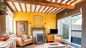 A cozy living room with a fireplace, wooden beams, a television, and a large window. - Traditional Cottage With Private Terrace (Durbuy)