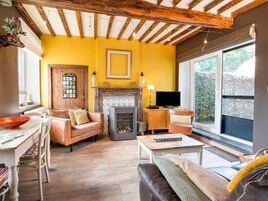 Una sala de estar acogedora con chimenea, vigas de madera, televisor y un ventanal grande.