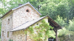 A stone building with a sloped roof, a small arched window, and a wooden porch. - Cottage in the Heart of the Ardennes Woods (Manhay)