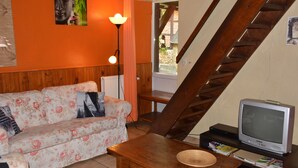 A living room with a sofa, a wooden table, a television, and a staircase. - Cottage in the Heart of the Ardennes Woods (Manhay)
