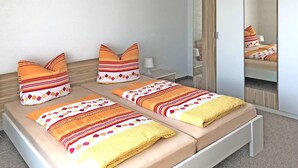 A double bed with patterned pillows and a yellow blanket, a bedside table with a lamp, and a mirror with a wooden frame. - Garden Apartment, Gobweinstein (Goessweinstein)