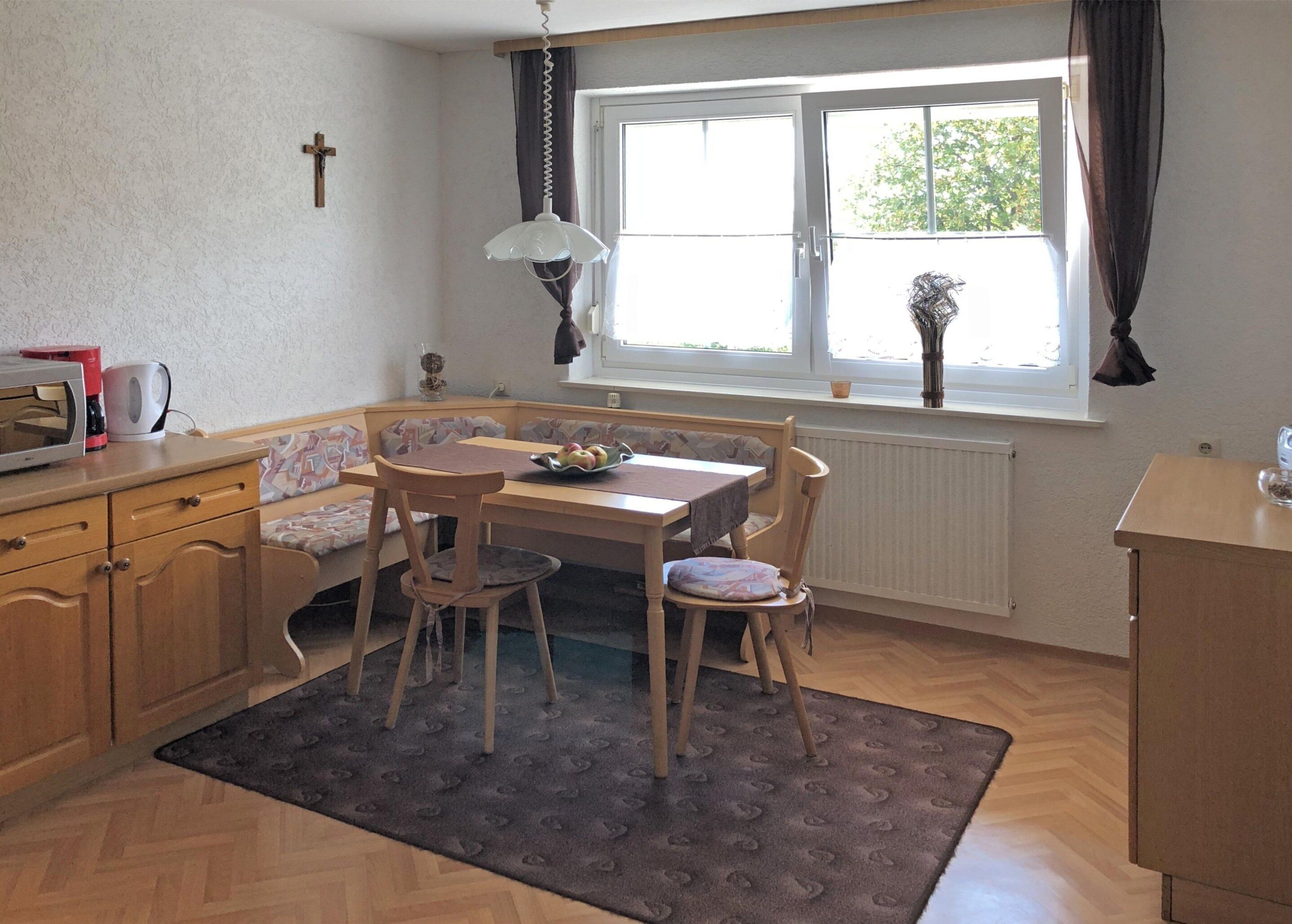 Una cocina acogedora con comedor, armarios de madera, microondas y ventana con cortinas.