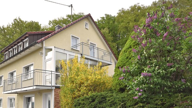 A two-story residential building with a balcony, a bench outside, and a car parked in front. - Garden Apartment, Gobweinstein (Goessweinstein)