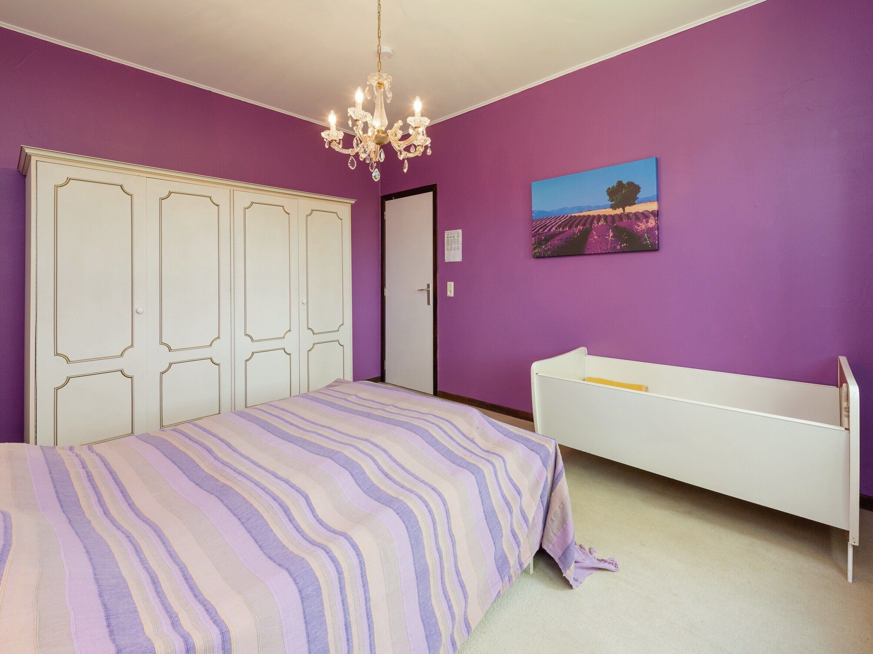 A bedroom with a bed, a crib, a chandelier, and a painting on the wall.