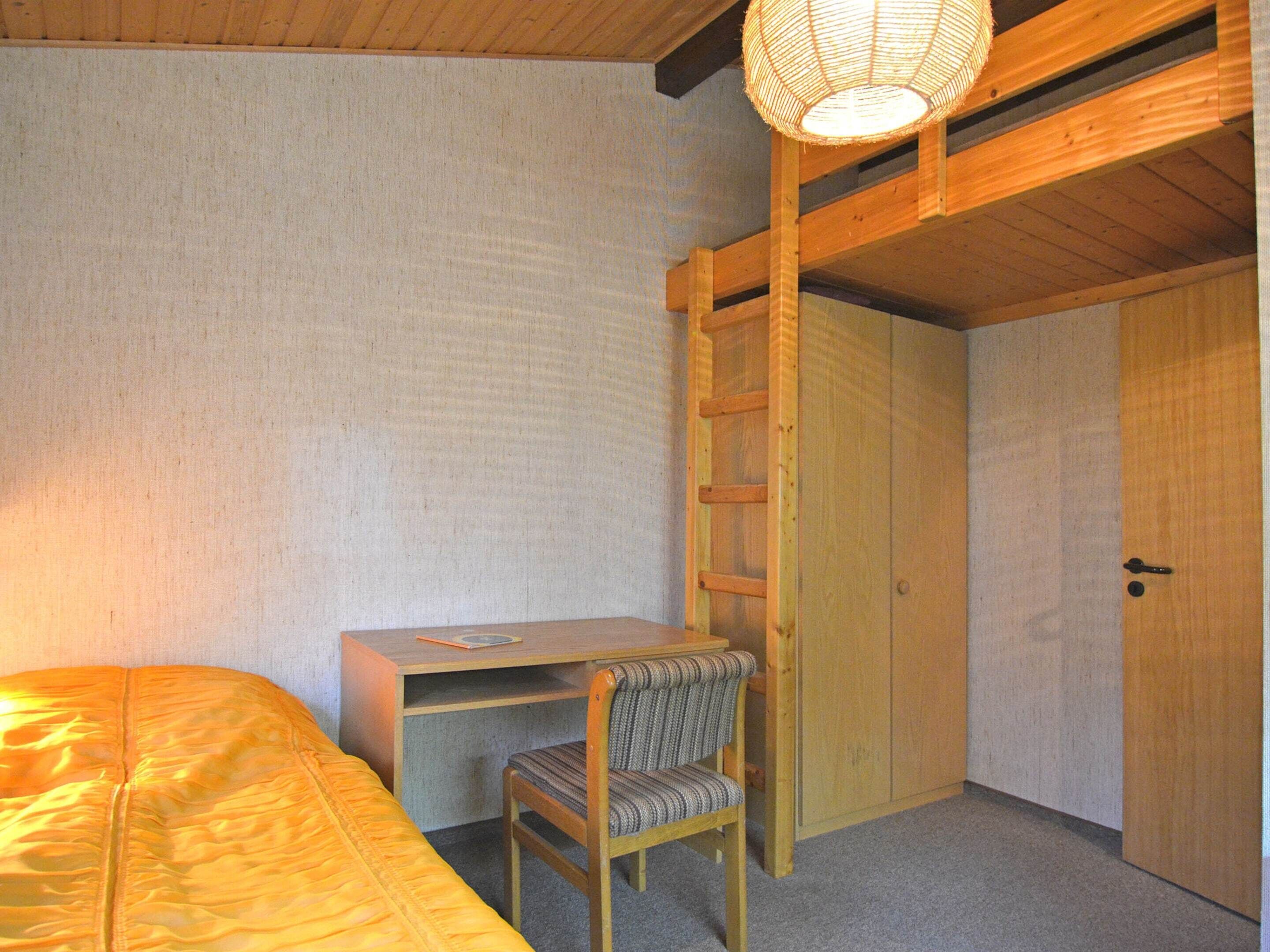 A small, cozy room with a bed, a desk, a chair, a ladder, and a wardrobe.