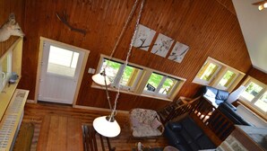 A spacious room with a wooden ceiling, a hanging light fixture, a sofa, a chair, and a stone wall. - Welcoming Cottage in Hatrival With Terrace (Saint-Hubert)