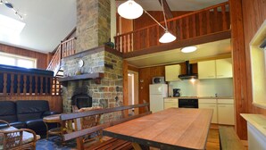 A cozy cabin interior with a stone fireplace, wooden dining table, and a lofted seating area. - Welcoming Cottage in Hatrival With Terrace (Saint-Hubert)