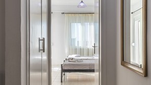 A hallway leading to a bedroom with a bed, a large mirror, and a door. - Comfy Central Square Gem with Terrace (Kalamata)