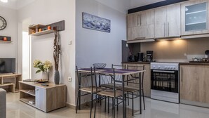 A modern kitchen with wooden cabinets, a built-in oven, and a dining area with a table and chairs. - Comfy Central Square Gem with Terrace (Kalamata)