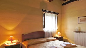 A bedroom with a bed, two bedside tables with lamps, a window with curtains, and a radiator. - Urban Farmhouse in Umbria With Pool (Monte Santa Maria Tiberina)