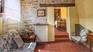 A cozy room with a stone wall, a wooden ceiling, a radiator, a sofa, a table with a vase, and a chair. - Urban Farmhouse in Umbria With Pool (Monte Santa Maria Tiberina)