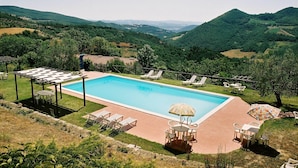 A swimming pool with a pergola, lounge chairs, and a table with an umbrella. - Urban Farmhouse in Umbria With Pool (Monte Santa Maria Tiberina)