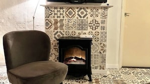 A room with a patterned floor, a sofa, a fireplace with a television above it, and a door. - Farmhouse in Nederweert Near Canal Trails (Nederweert-Eind)