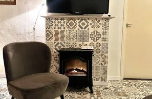 Una habitación con suelo estampado, un sofá, una chimenea con un televisor encima y una puerta.
