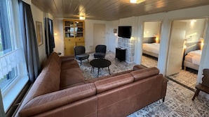 A modern hotel room with a brown leather sofa, a small black table, two armchairs, a TV mounted on a cabinet, and a patterned rug. - Farmhouse in Nederweert Near Canal Trails (Nederweert-Eind)