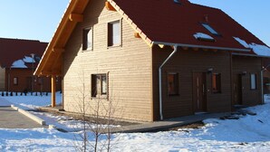 A two-story wooden house with a red roof, multiple windows, and a visible chimney. - Ferienhaus in Hasselfelde (Oberharz am Brocken)
