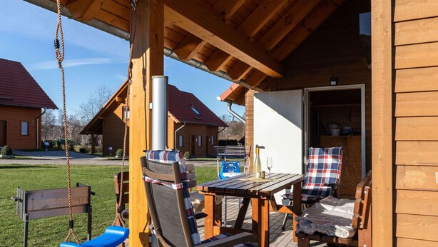 A wooden deck with outdoor seating, a swing set, and a table with a bottle and glass. - Ferienhaus in Hasselfelde (Oberharz am Brocken)