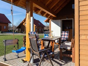 A wooden deck with outdoor seating, a swing set, and a table with a bottle and glass. - Ferienhaus in Hasselfelde (Oberharz am Brocken)