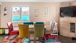 A modern living room with a dining area, a large window with a view, a flat-screen TV, and a cabinet with glass doors. - Ferienhaus in Hasselfelde (Oberharz am Brocken)