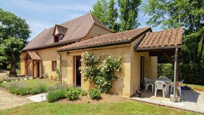 A two-story house with a tiled roof, a covered patio with a table and chairs, and a garden with various plants. - Cozy Cottage Retreat in Vezac (Vezac)