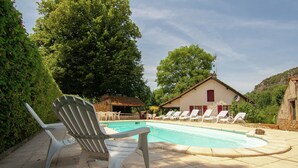A swimming pool with lounge chairs, a building with a red door, and a stone wall. - Cozy Cottage Retreat in Vezac (Vezac)