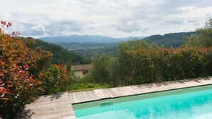 A swimming pool with a wooden deck, surrounded by lush greenery and a view of distant mountains. - Belvilla by OYO Casa Luna (Pescia)