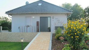 A single-story building with a tiled roof, a front door, and a small garden with yellow flowers. - Woodland Escape With Garden (Neunburg vorm Wald)