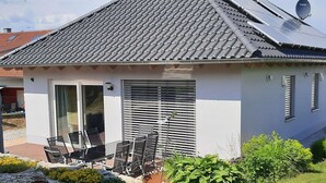 A small house with a tiled roof, a sliding glass door, and a patio with chairs and a table. - Woodland Escape With Garden (Neunburg vorm Wald)