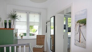 A hallway with a wicker chair, a large mirror, and a view of the outdoors through a window. - Cozy Apartment in Neubukow near Water Sports (Neubukow)