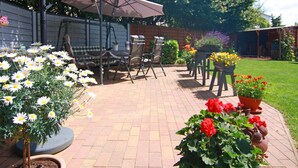A patio with a swing set, a table, and chairs. There are potted plants and flowers around the patio. - Cozy Apartment in Neubukow near Water Sports (Neubukow)