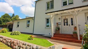 A two-story house with a porch, a front door, and a small garden with a stone border. - Cozy Apartment in Neubukow near Water Sports (Neubukow)