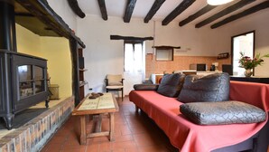 A cozy living room with a fireplace, a sofa, a table, and a kitchen area in the background. - Romantic Cottage, Berbiguieres (Allas-les-Mines)