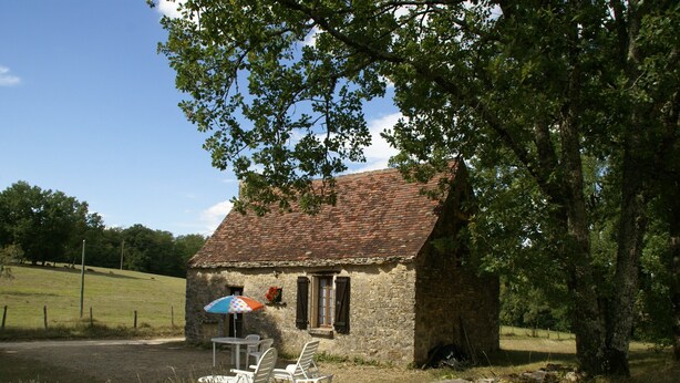 A stone cottage with a tiled roof, a small table with chairs, and a blue umbrella. - Romantic Cottage, Berbiguieres (Allas-les-Mines)