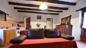 A room with a red sofa, wooden beams, a kitchen with appliances, and a framed picture on the wall. - Romantic Cottage, Berbiguieres (Allas-les-Mines)