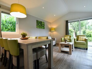 Un salon moderne comprenant un coin repas, des chaises vertes, une table en bois et une grande fenêtre donnant sur un paysage verdoyant.