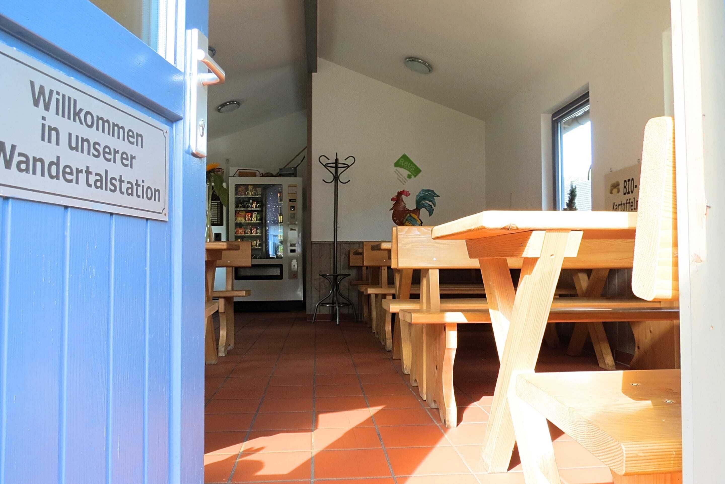 Uma área com bancos de madeira e uma placa com a inscrição 'Willkommen in unserer Wandertalstation'.