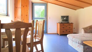 A room with a wooden ceiling, a television on a wooden cabinet, a bed, and a window with a view of greenery. - Charmante Wohnung mit Eigener Terrasse (Bad Wildungen)
