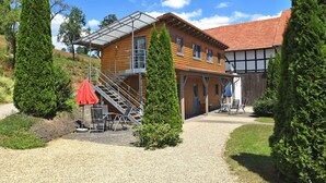 A two-story wooden house with a red-tiled roof, a covered outdoor seating area, and a gravel driveway. - Charmante Wohnung mit Eigener Terrasse (Bad Wildungen)