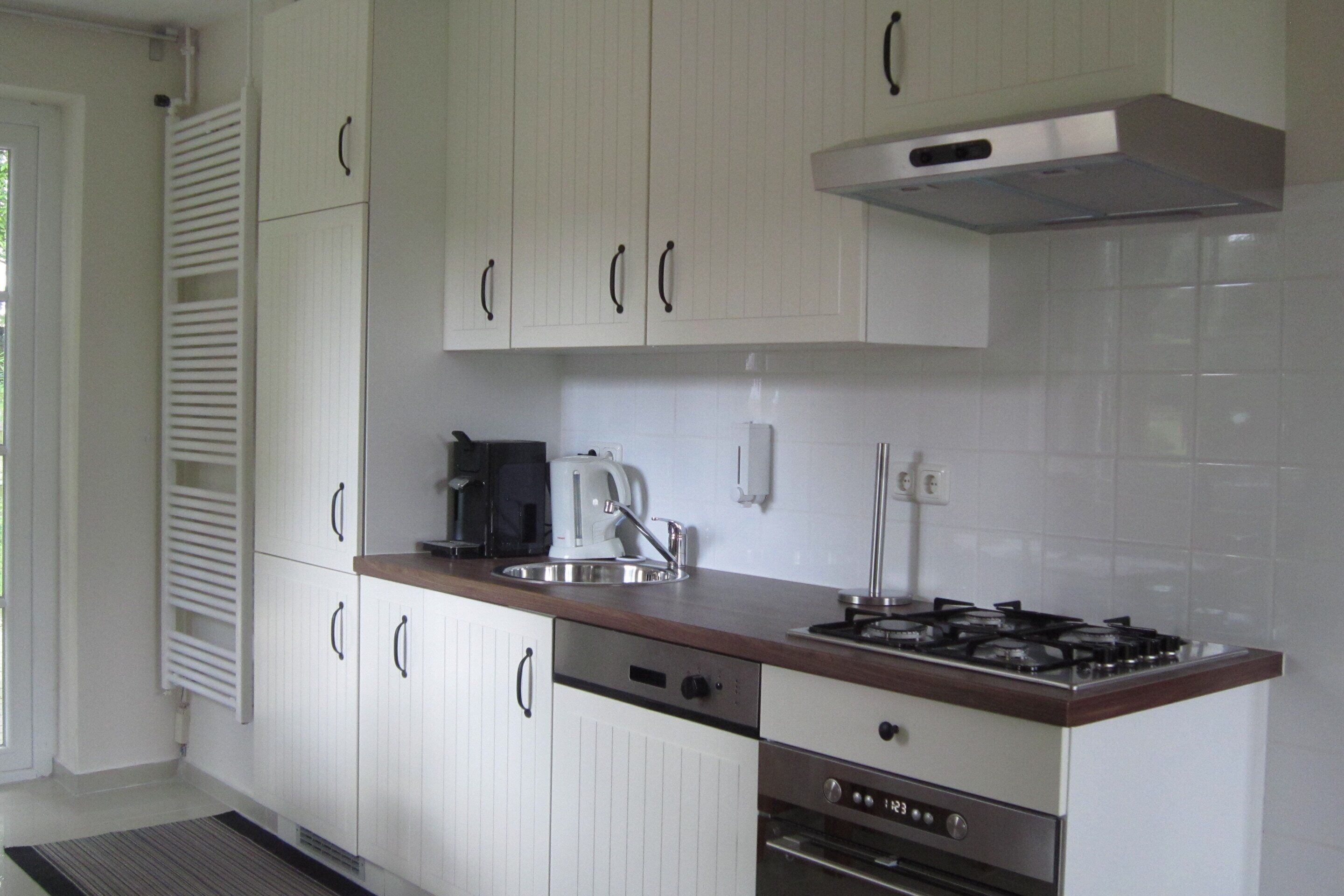Una cocina moderna con armarios blancos, estufa de acero inoxidable y cafetera.