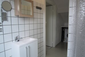 A bathroom with white tiles, a sink, a mirror, and a washing machine in the background. - Holiday Home in Spijk With Meadow Views (Spijk)