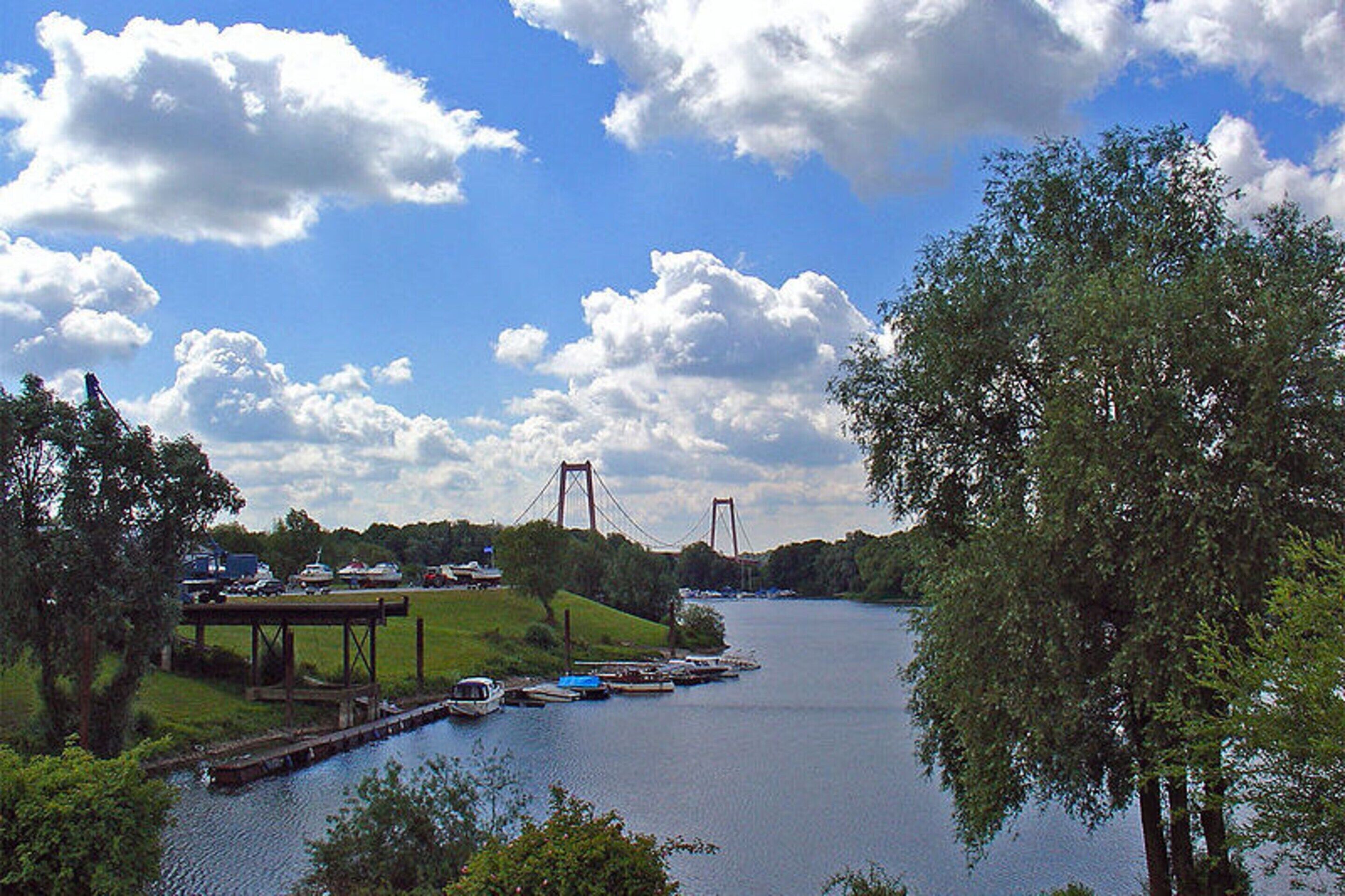 A river with a bridge, boats docked, and a grassy area with trees.