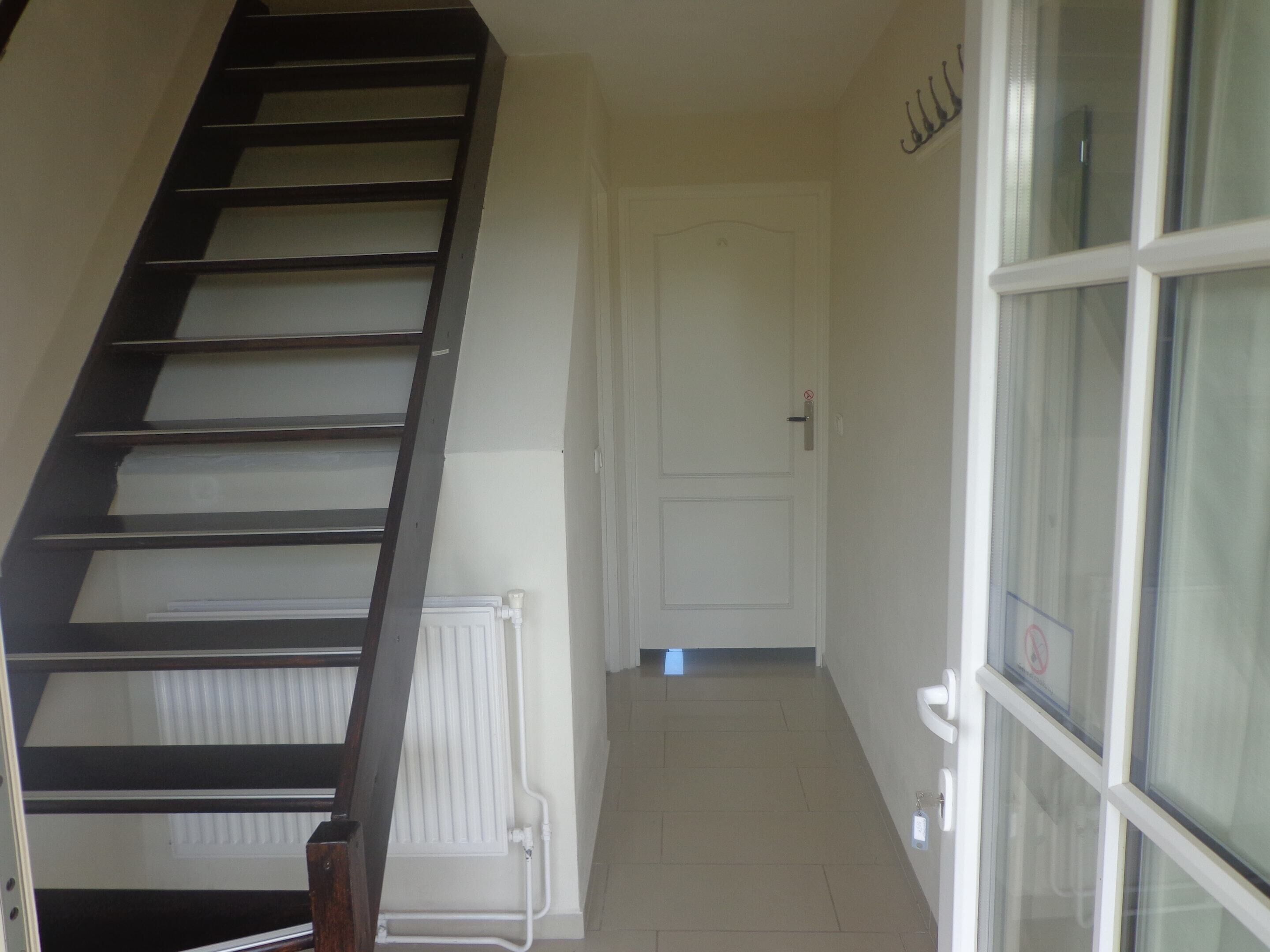 Un escalier menant à un palier où se trouve une porte blanche et une fenêtre avec un vitrage dépoli.